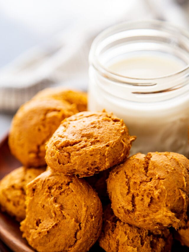 pumpkin cookies stacked on wood plate with glass of milk
