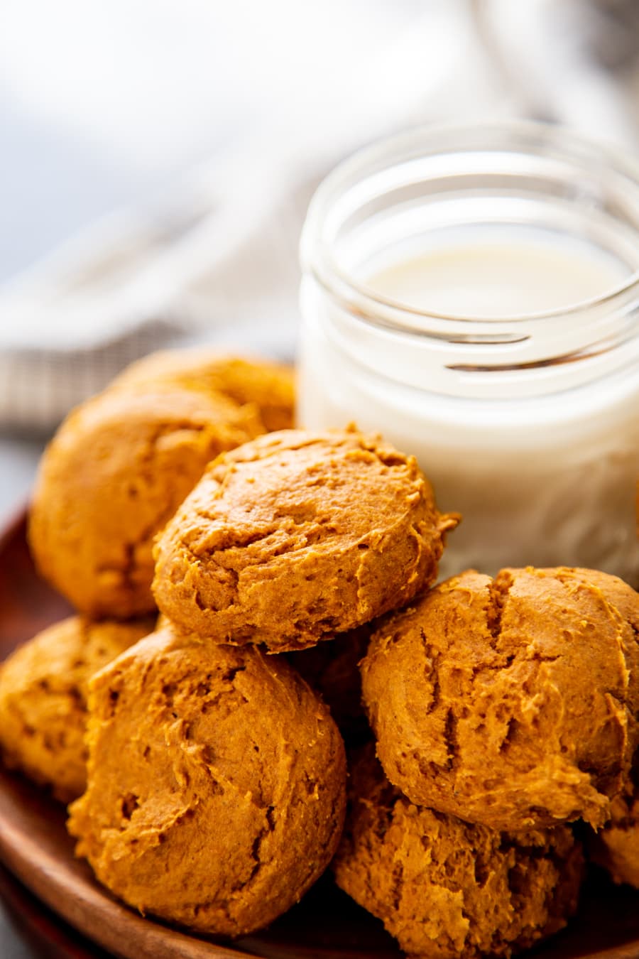 pumpkin cookies stacked on wood plate with glass of milk