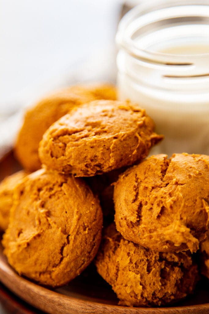 pumpkin cookies stacked on wood plate with glass of milk