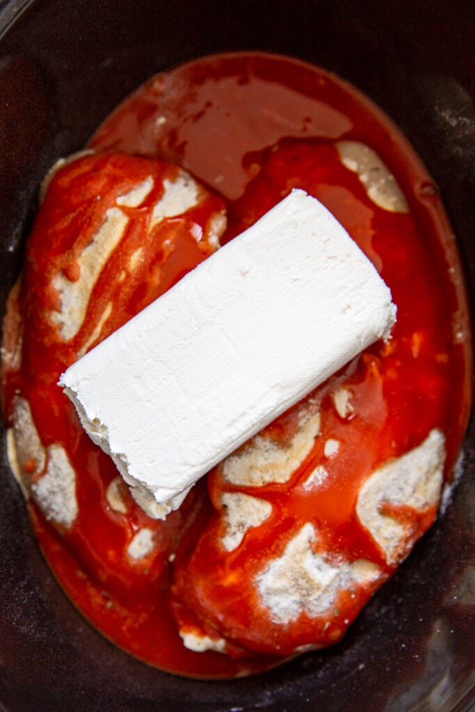 overhead shot of chicken breasts with cream cheese and buffalo sauce in slow cooker