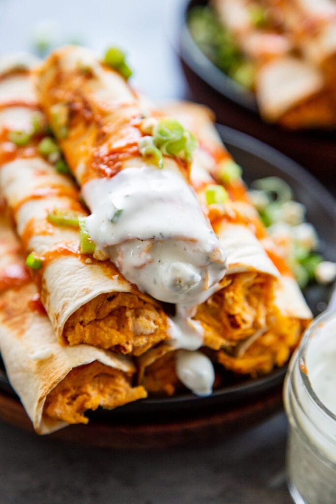 stack of taquitos with the topped one dipped in blue cheese and ranch