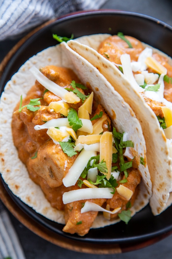 tacos with chicken topped with cheese and cilantro on black plate