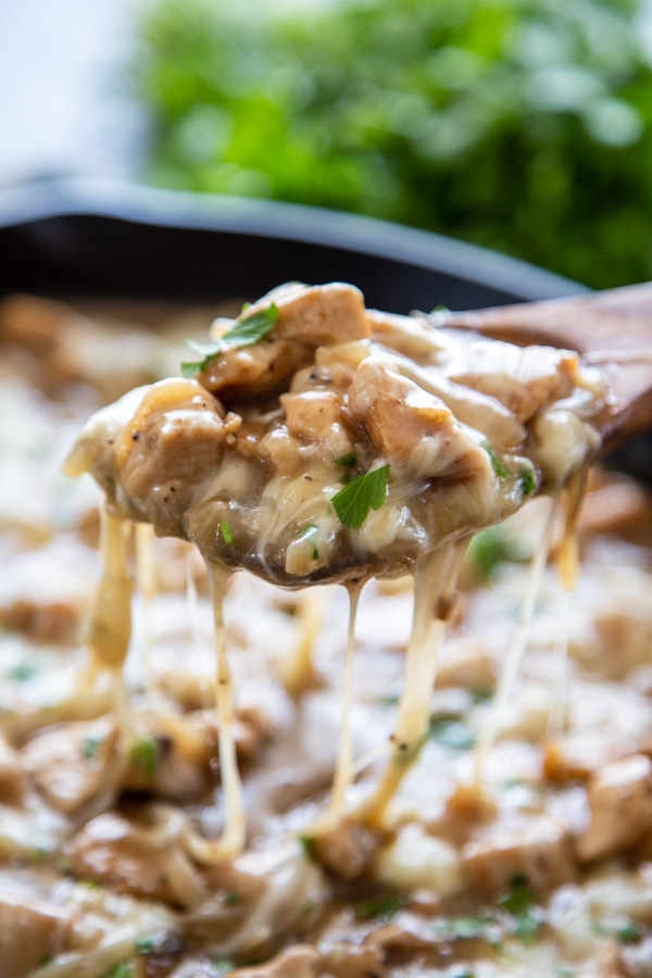 serving spoon of overhead shot of skillet with chicken, cheese and french onion soup