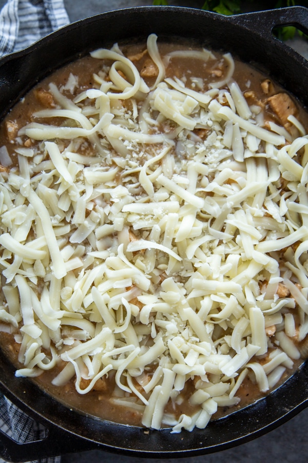 overhead shot of chicken in skillet with seasonings, soup and cheese