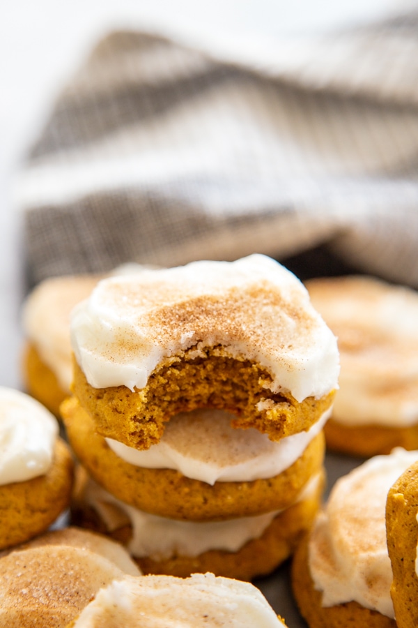 stack of frosted pumpkin cookies with one cookie with a bite taken out