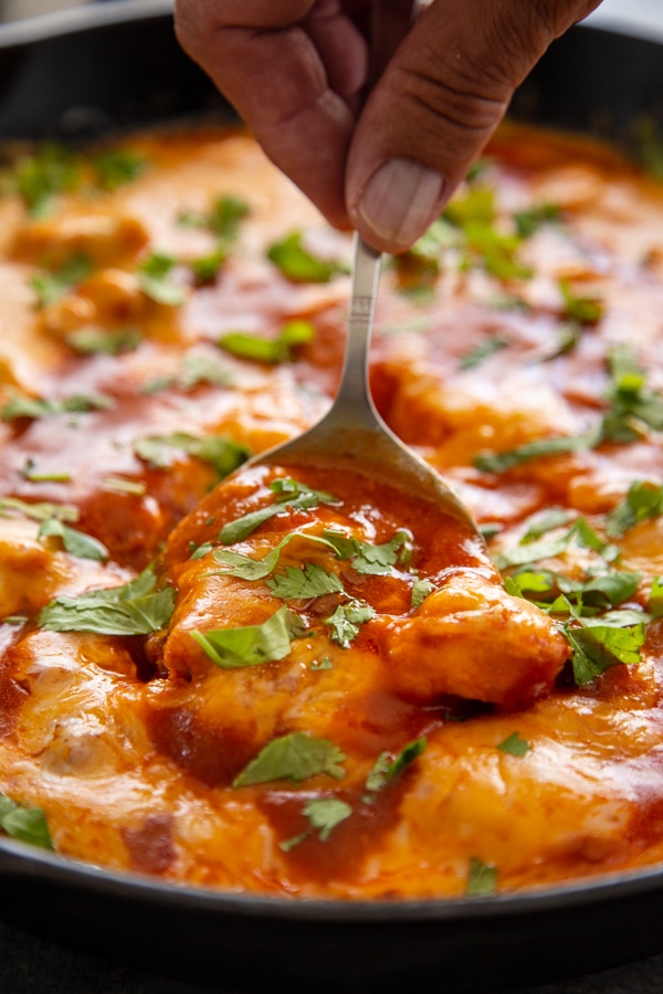 salsa chicken in skillet with hand on metal spoon, scooping from the skillet