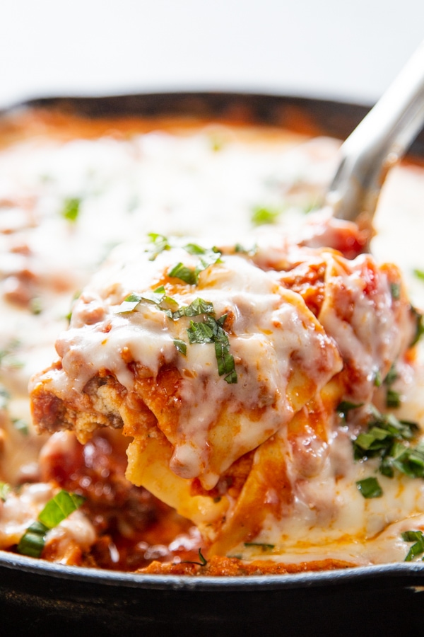 serving spoon topped with lasagna being pulled out of the skillet