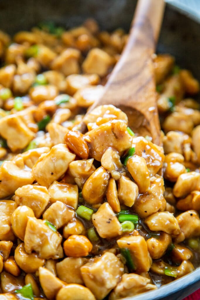 close up shot of cashew chicken in skillet with wooden spoon