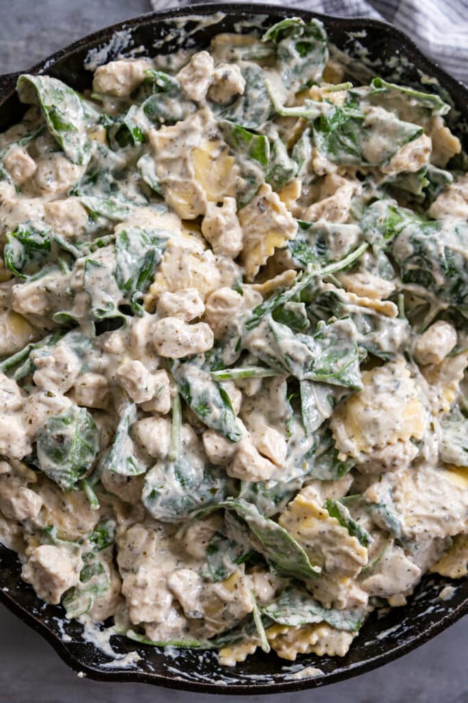 overhead shot of skillet with creamy pesto sauce an spinach and ravioli
