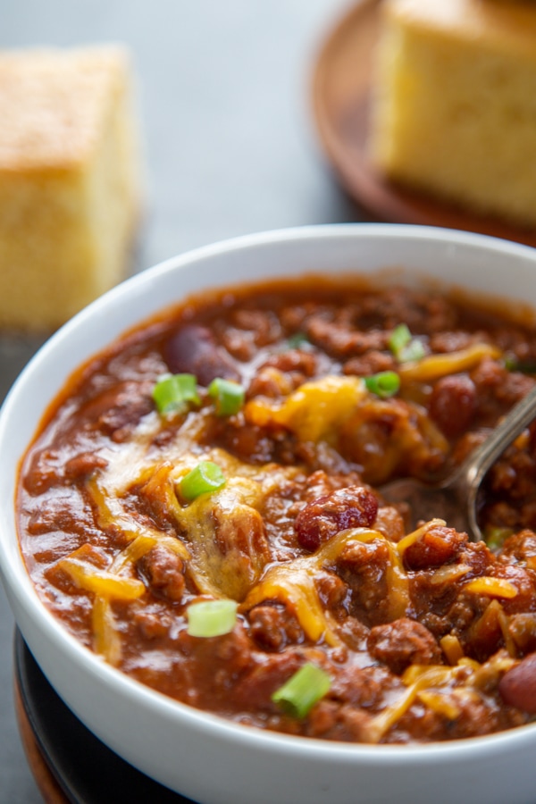 white bowl of chili with cheese and spoon