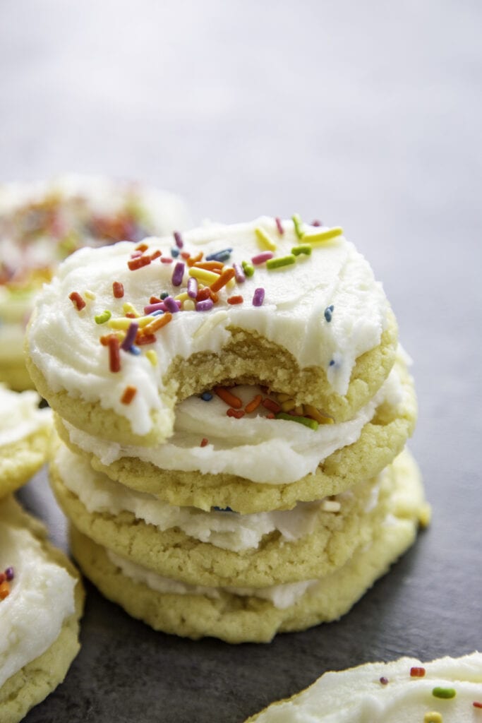 stack of frosted sugar cookies with sprinkles with bite taken out of one