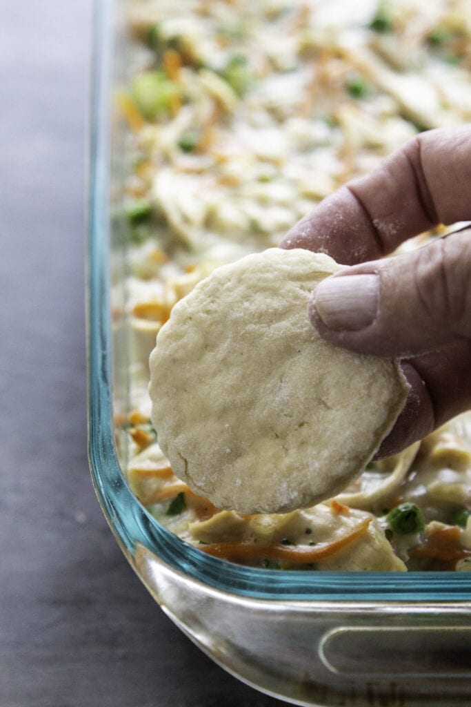 raw biscuit being placed on top of chicken pot pie filling in baking pan