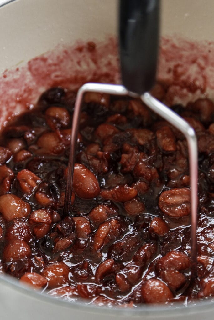 potato masher smashing grapes and cranberries in white pot