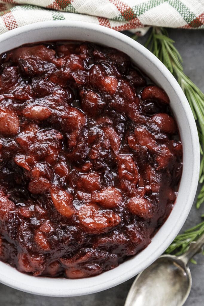 cranberry grape compote in a white bowl with rosemary as a garnish and Christmas napkin