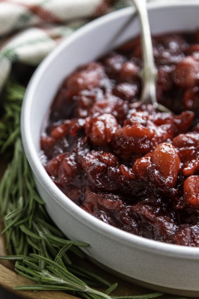 cranberry compote in a white bowl with rosemary as a garnish side view with silver spoon