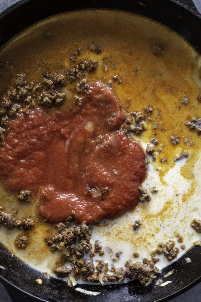 overhead shot of skillet with hamburger, tomato sauce, milk and onions