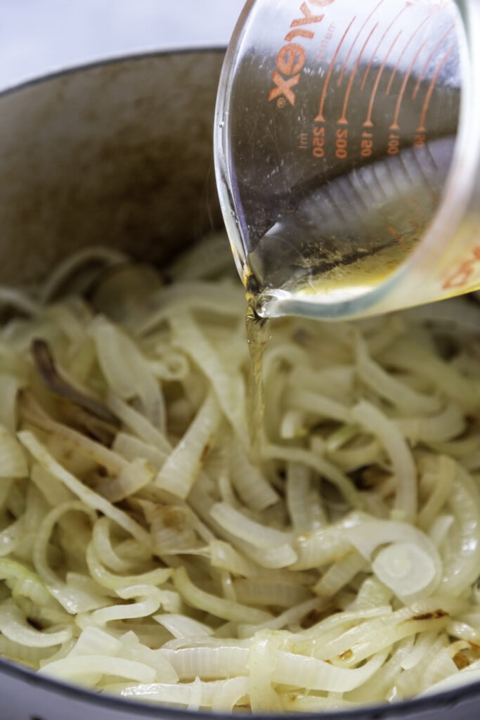 broth being poured over onions in pot