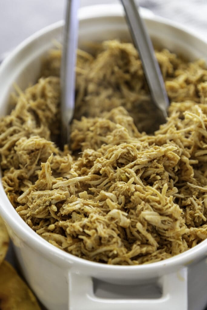 shredded chicken in white pot with tongs