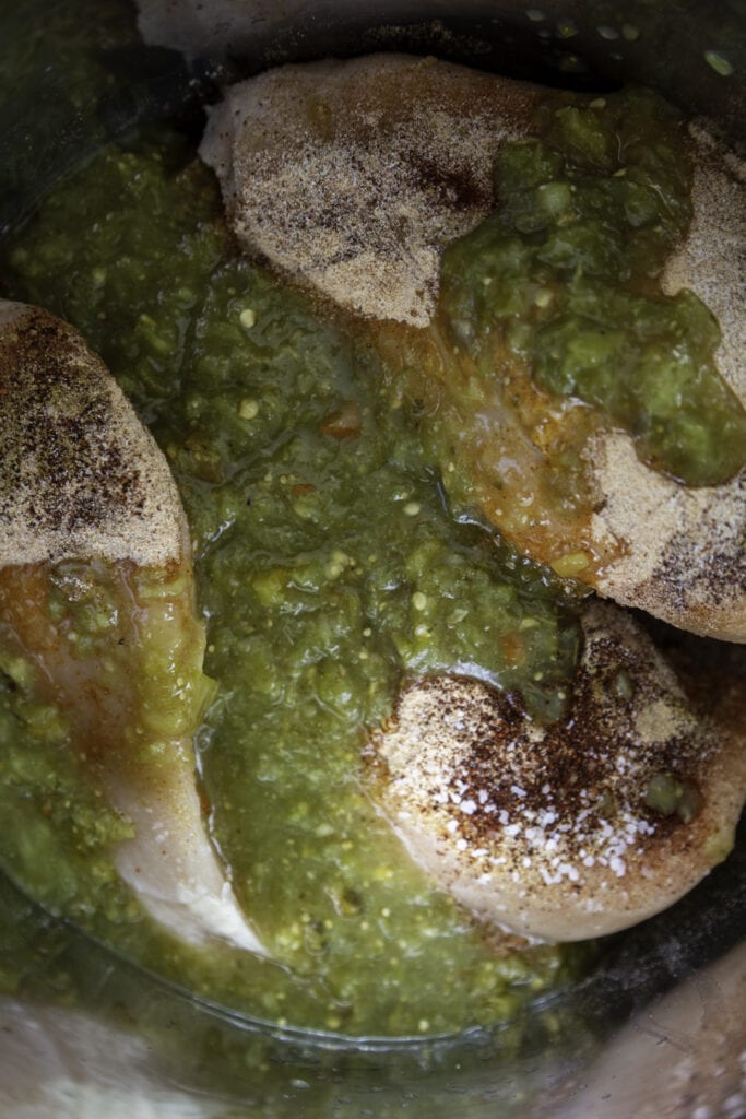 overhead shot of chicken in seasonings and green salsa poured over them
