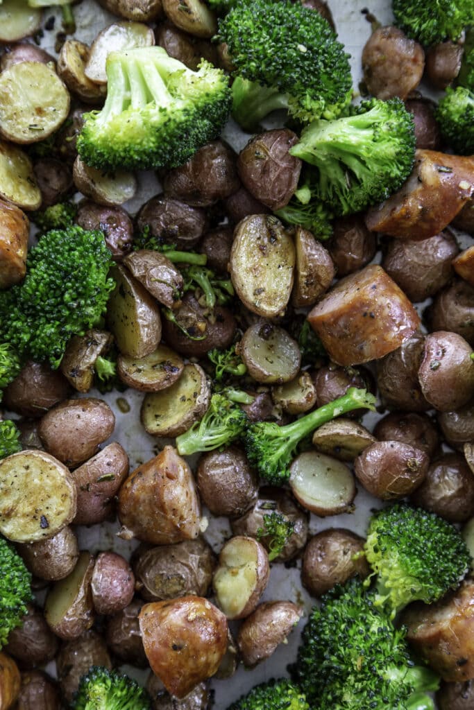 overhead shot of cooked sausages, potatoes and broccoli on baking sheet