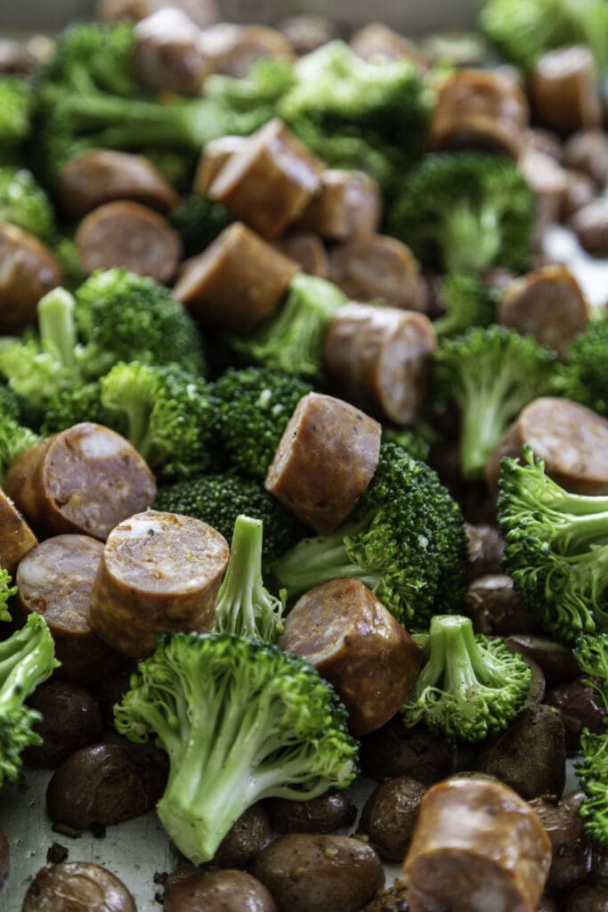 sausages cut and broccoli on baking sheet