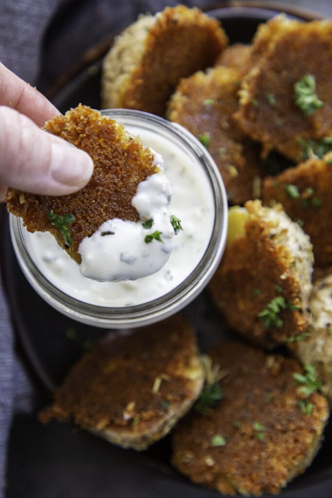 overhead shot of rosemary parmesan crusted potatoes with potato being dipped into the sauce