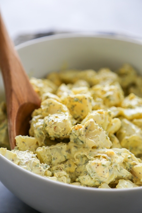 potato salad in white serving bowl with wooden serving spoon