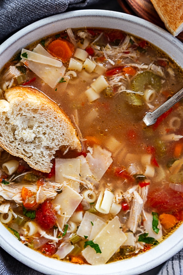 overhead shot of chicken soup in white bowl with piece of french bread