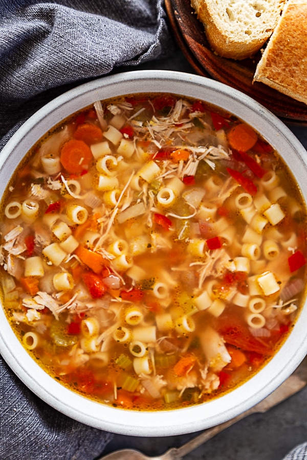 overhead shot of siclian chicken soup in white bowl with french bread on the side