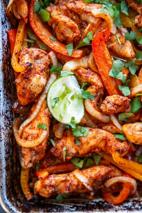 corner shot of sheet pan with chicken fajitas on it with lime