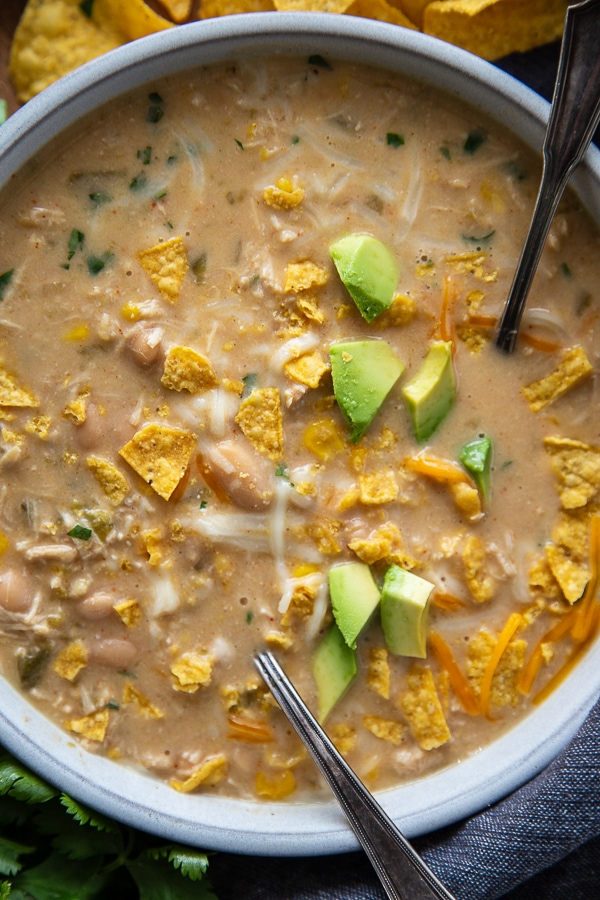 overhead shot of white chicken chili in bowl with chopped avocados and chips with 2 spoons