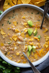 overhead shot of white chicken chili in bowl with chopped avocados and chips