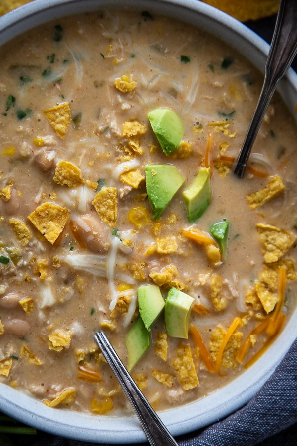 close up overhead shot of white chicken chili in bowl with chopped avocados and chips