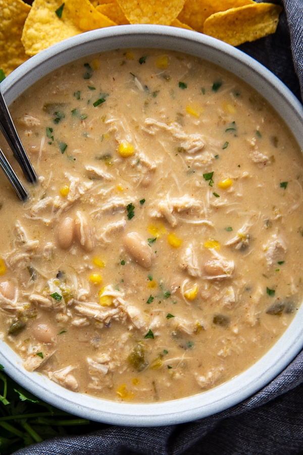 overhead shot of white chicken chili in bowl with chips on the side and two spoons