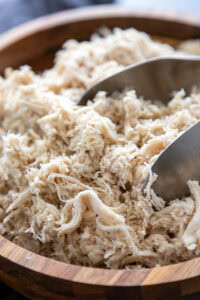 bowl of shredded chicken with tongs